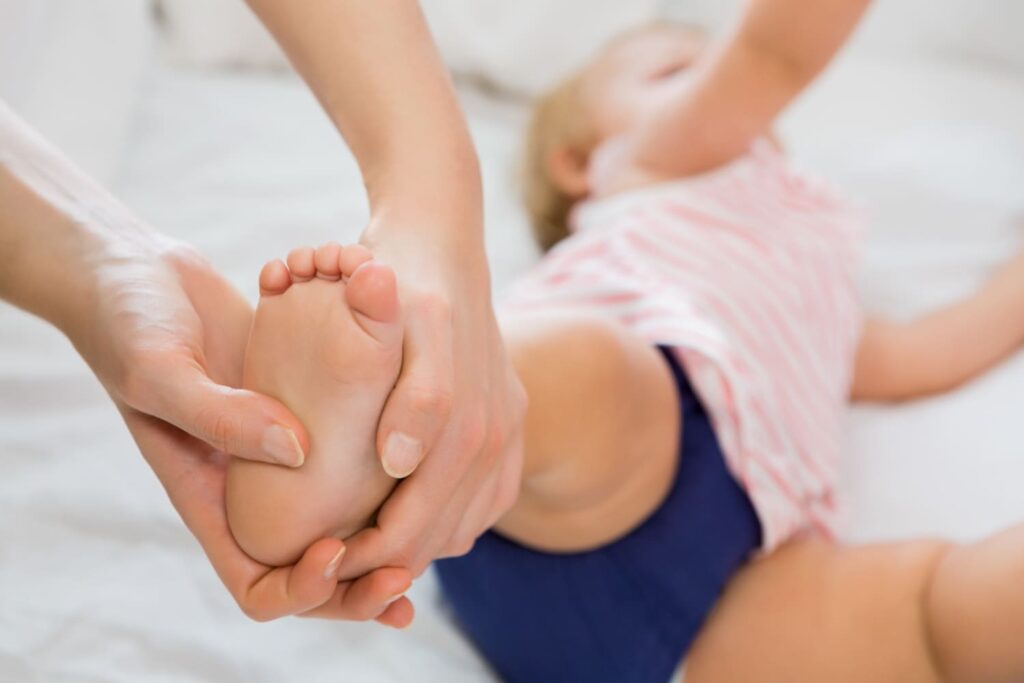 fisioterapeuta estirando piernas de nino pequeno en sesion de terapia en ambiente clinico