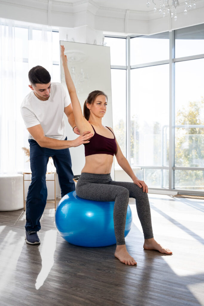 terapeuta ayudando a paciente a realizar ejercicio de estiramiento sentado en bola de fitness